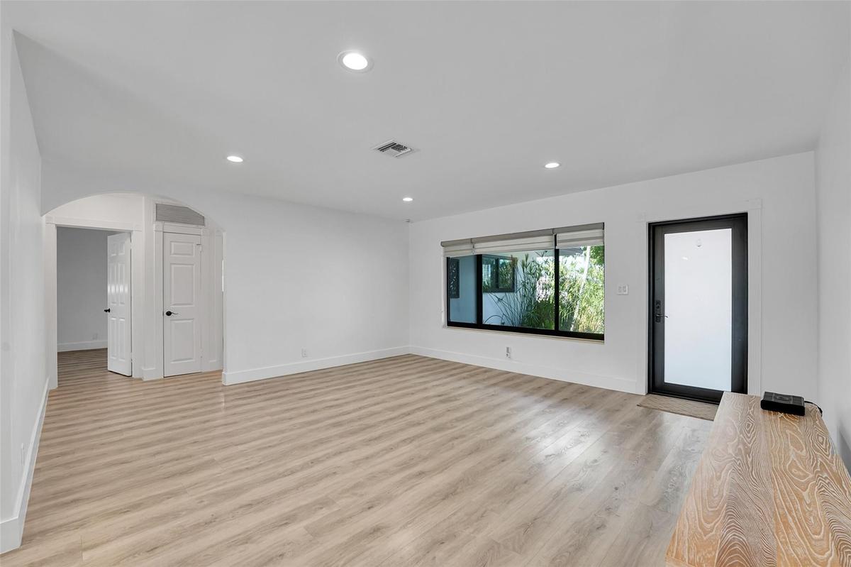 Recessed lighting, light wood-finish flooring, white walls, arched doorway, and a modern entry door with frosted glass