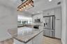 Kitchen featuring a stone-finish island with seating, a five-light linear chandelier, stainless steel appliances, light-toned cabinetry, and wood-fini