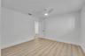 Wood-finish flooring, white walls, white ceiling fan with integrated lighting, and a white paneled door