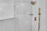 Shower enclosure with floor-to-ceiling glass panel, large format tile, decorative accent tile, built-in shelf, and a gold-toned shower system