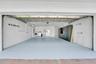 Expansive garage with light-toned flooring, built-in cabinetry, overhead structural elements, and a wall-mounted window