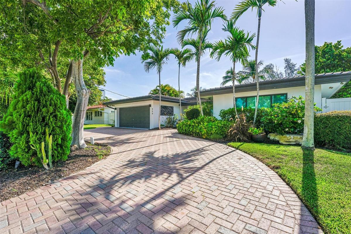 Brick paver driveway with mature tropical landscaping, including palm trees and established shrubs