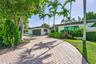 Brick paver driveway with mature tropical landscaping, including palm trees and established shrubs