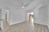 Light wood-finish flooring, white walls, modern ceiling fan with integrated lighting, and multiple doorways