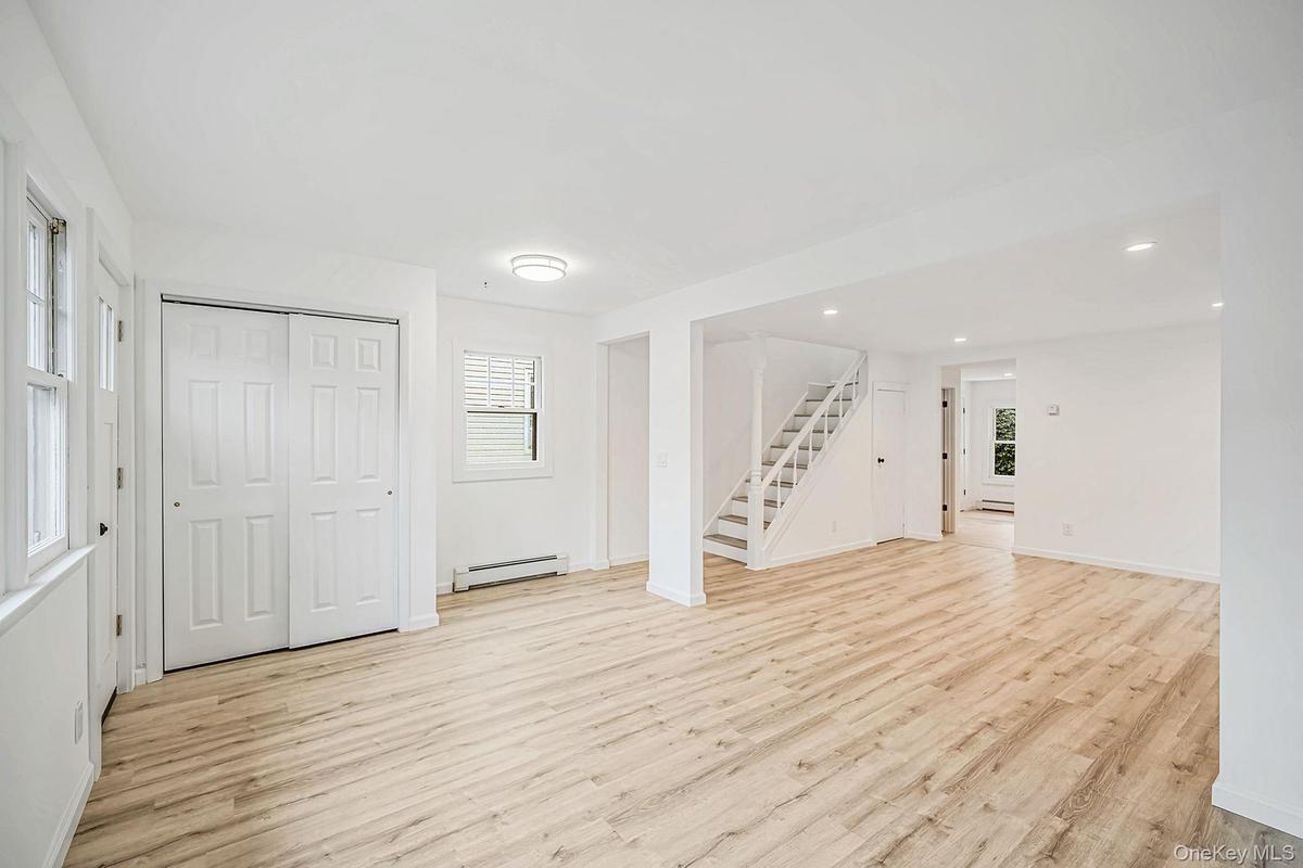 Open-concept interior featuring light-tone wood-finish flooring, recessed lighting, double-panel closet doors, and a staircase with white balusters