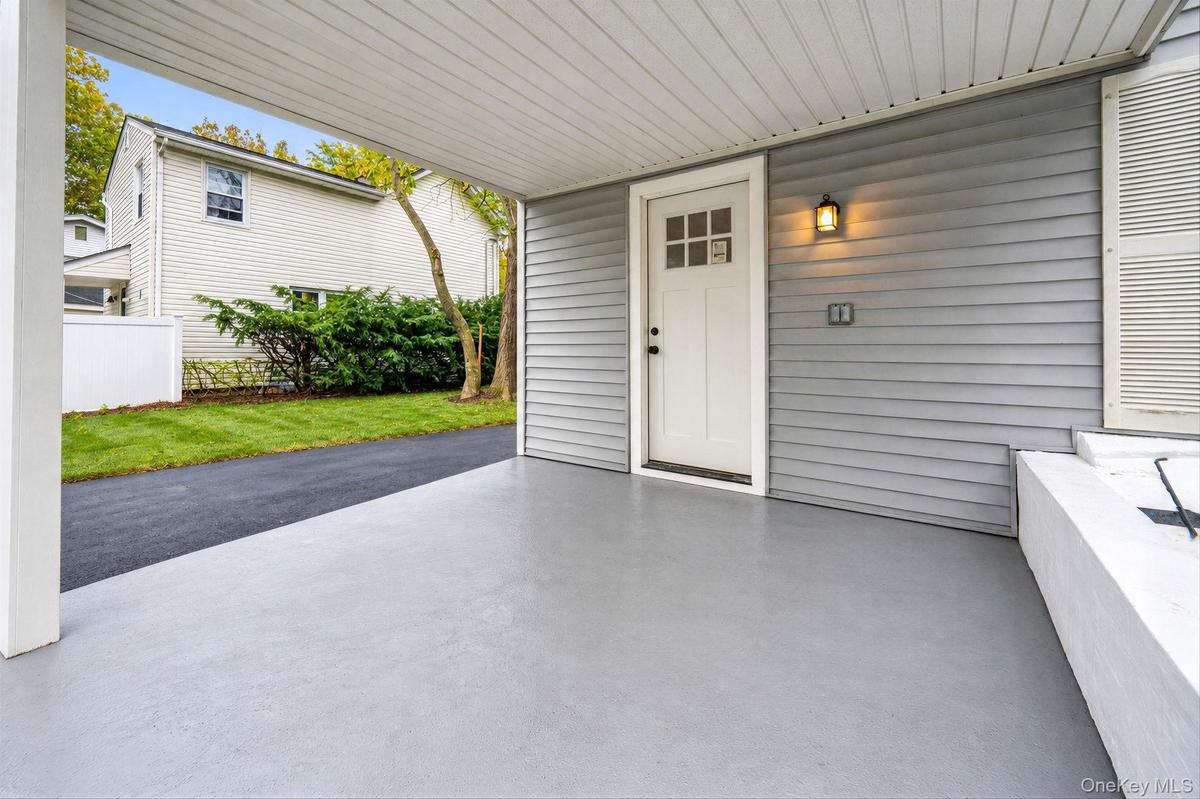 Covered carport featuring gray siding, a painted concrete floor, a six-pane window exterior door, and a wall-mounted light fixture