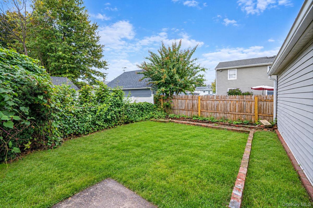 Private backyard featuring a fenced perimeter, brick-edged garden beds, and mature landscaping *virtually edited