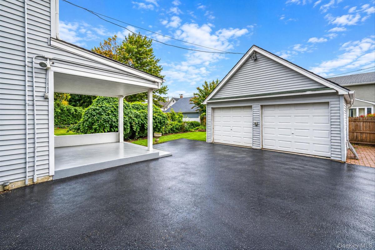 Exterior space featuring a covered patio, two-car detached garage with white overhead doors, and asphalt driveway