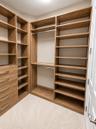 Custom walk-in closet featuring wood-finish cabinetry, built-in shelving, integrated dresser drawers with metal pulls, and dual hanging rods