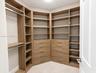 Walk-in closet featuring custom wood-finish built-in shelving, multiple integrated storage drawers, brushed metal hardware, and hanging rods