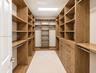 Walk-in closet featuring custom wood-finish built-in shelving, integrated dresser drawers with metallic hardware, multiple garment rods, and recessed 