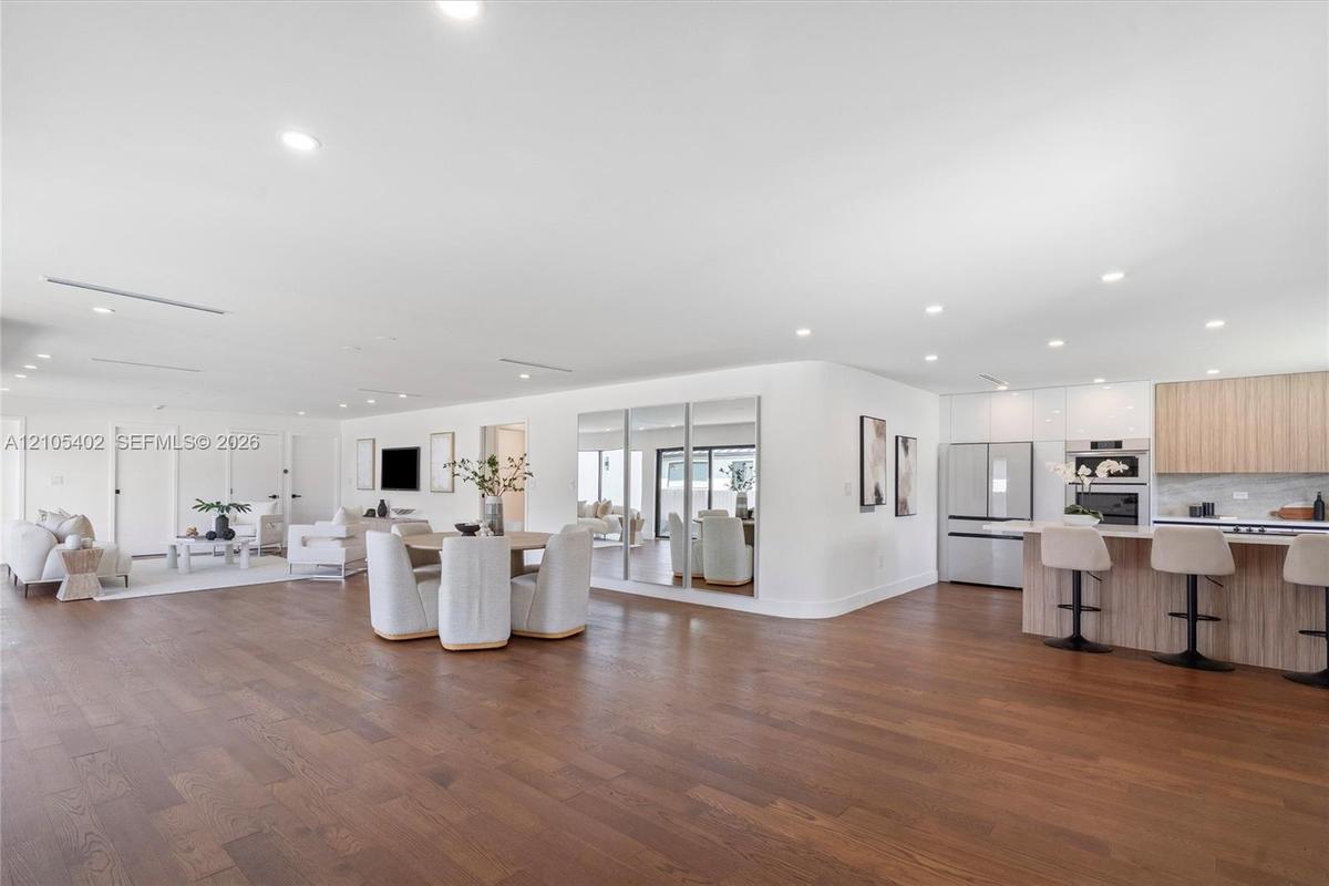 Open-concept interior featuring wood-finish flooring, recessed lighting, a built-in mirrored wall, and a kitchen equipped with wood-finish cabinetry a