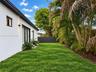 Exterior featuring white stucco siding, black-framed glass sliding doors, dark metal wall-mounted exterior lighting, manicured lawn, and mature palm t