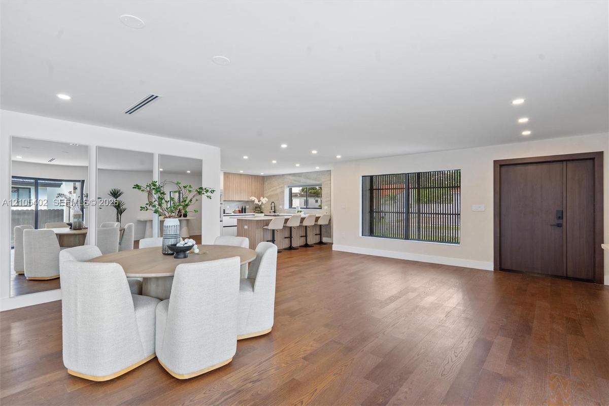 Open-concept interior featuring wood-finish flooring, recessed lighting, a built-in wall mirror, and a solid wood front door