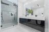 Floating high-gloss black vanity featuring a dual-sink white countertop, wall-to-wall mirror, glass-enclosed walk-in shower with stone-finish wall til