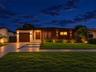 Modern single-story exterior featuring a wood-panel façade, integrated wall sconce lighting, solid wood front door, horizontal-slat garage door, and c