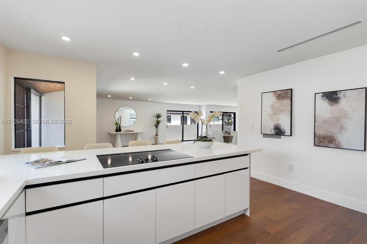 Kitchen island featuring white flat-panel cabinetry, a solid surface countertop, and an integrated cooktop, complemented by recessed lighting and wood