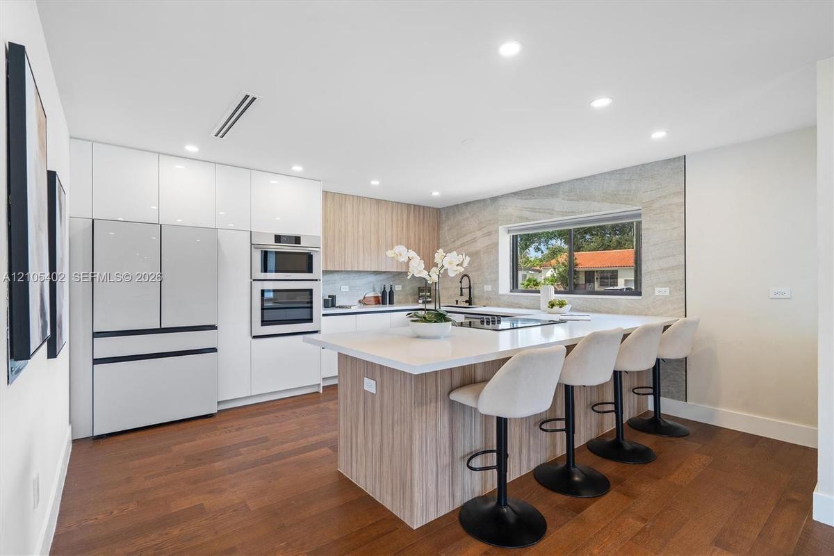 Kitchen featuring flat-panel cabinetry, a central island with a solid surface countertop, wood-finish flooring, integrated wall ovens, and a stone-sty