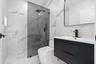 Modern bathroom featuring large-format wall and floor tile with a veined pattern, walk-in shower with glass panel, matte black plumbing fixtures, and 