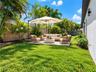 Private backyard featuring a level grass lawn, mature tropical landscaping, and a wood privacy fence