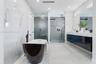 Freestanding deep-soaking tub with floor-mounted matte black faucet, wall-to-wall stone-finish tile surround, wall-mounted floating dual vanity with i