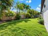 Landscaped backyard featuring a manicured lawn, wood-panel fencing, mature palm trees, and exterior wall-mounted light fixtures