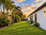 Expansive backyard featuring a manicured lawn, mature palm trees, exterior wall-mounted lighting, and privacy fencing