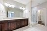 Double vanity featuring dark wood-finish cabinetry, stone-surface countertop, dual undermount sinks, and a large-format vanity mirror with dual light 