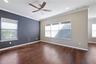 Wood-finish flooring, charcoal accent wall, crown molding, recessed lighting, and ceiling fan with integrated lighting