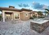Covered terrace featuring stone paver flooring, outdoor kitchen with stone veneer base and stone countertop, and double-door entry