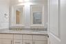 Dual-vanity cabinet featuring white shaker-style cabinetry, speckled stone countertop, integrated undermount sinks, and two framed wall mirrors with t