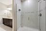 Walk-in shower with a glass enclosure, tile surround, and metallic fixtures, featuring a vanity with stone-finish countertop, dark wood cabinetry, and