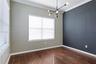 Room featuring wood-finish flooring, a dark accent wall, crown molding, and a contemporary multi-arm chandelier