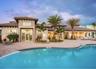 Stucco exterior featuring a multi-tiered tile roof, covered patio area, brick-paver pool deck, and freeform swimming pool with integrated landscaping