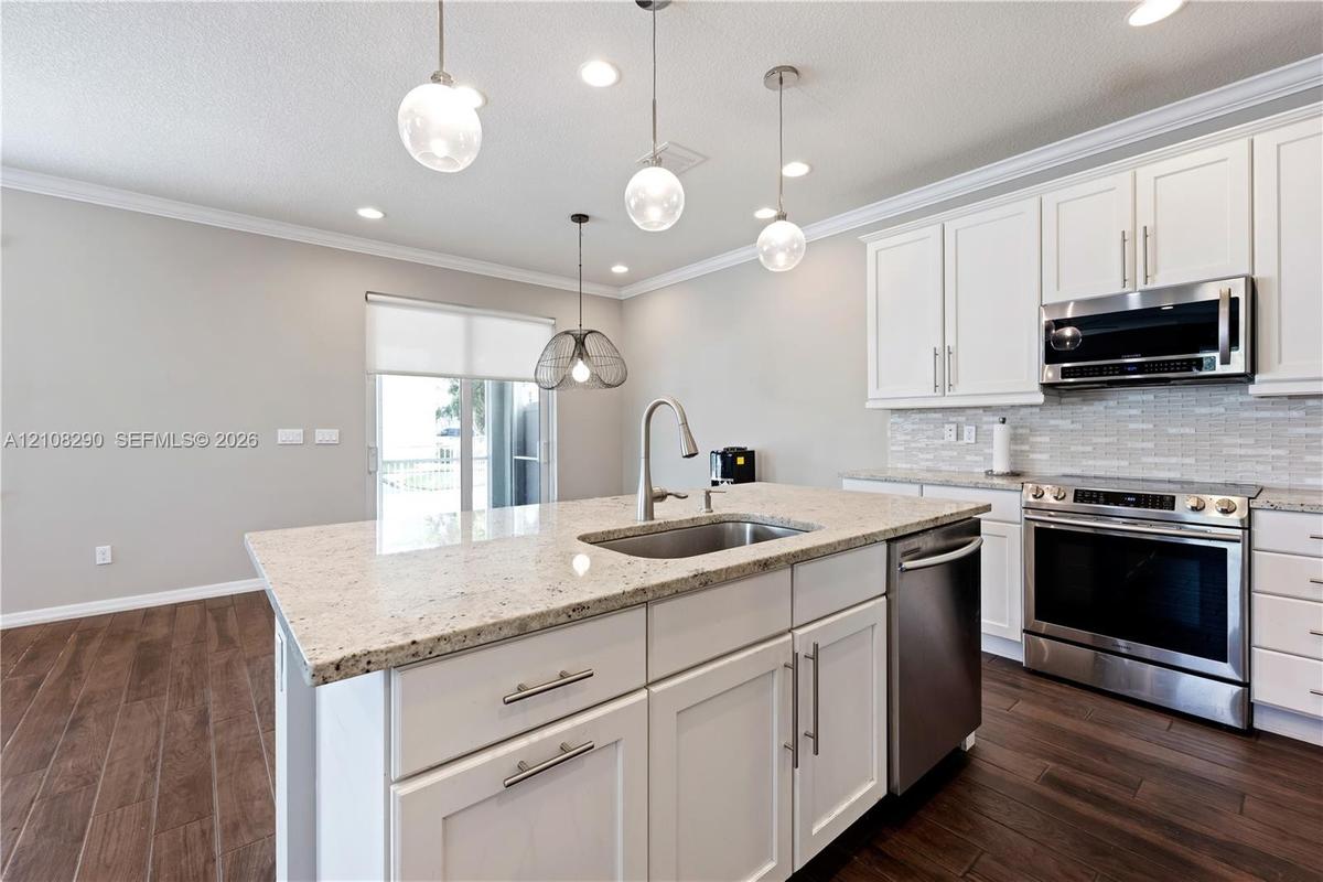 Kitchen featuring white shaker-style cabinetry, stone countertops, stainless steel appliances, wood-finish flooring, and multi-pendant lighting