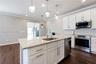 Kitchen featuring white shaker-style cabinetry, stone countertops, stainless steel appliances, wood-finish flooring, and multi-pendant lighting