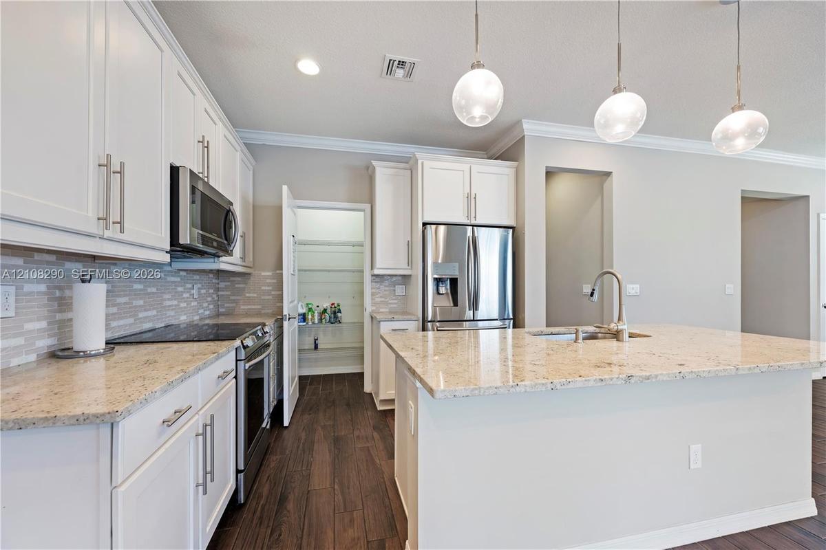Kitchen featuring white shaker-style cabinetry, stone countertops, stainless steel appliances, wood-finish flooring, and three glass pendant lights ov