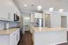 Kitchen featuring white shaker-style cabinetry, stone countertops, stainless steel appliances, wood-finish flooring, and three glass pendant lights ov