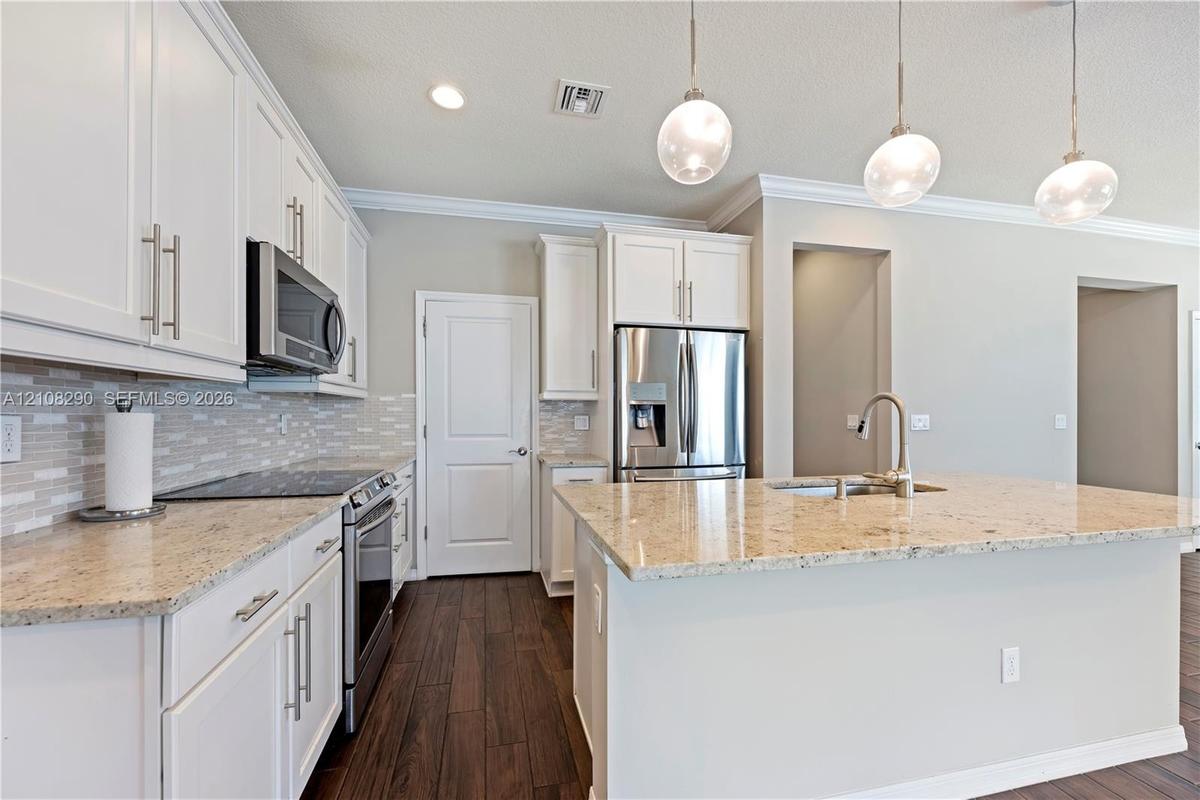 Kitchen featuring white shaker-style cabinetry, stone countertops, stainless steel appliances, decorative glass pendant lighting, and wood-finish floo