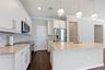Kitchen featuring white shaker-style cabinetry, stone countertops, stainless steel appliances, decorative glass pendant lighting, and wood-finish floo