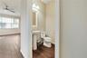 Pedestal sink with a polished metal faucet, multi-light fixture, white toilet, and wood-finish tile flooring