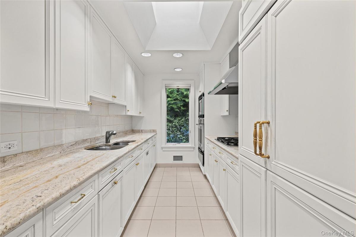 Kitchen featuring white cabinetry, stone countertops, integrated double wall ovens, a skylight, and large-format tile flooring
