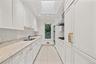 Kitchen featuring white cabinetry, stone countertops, integrated double wall ovens, a skylight, and large-format tile flooring