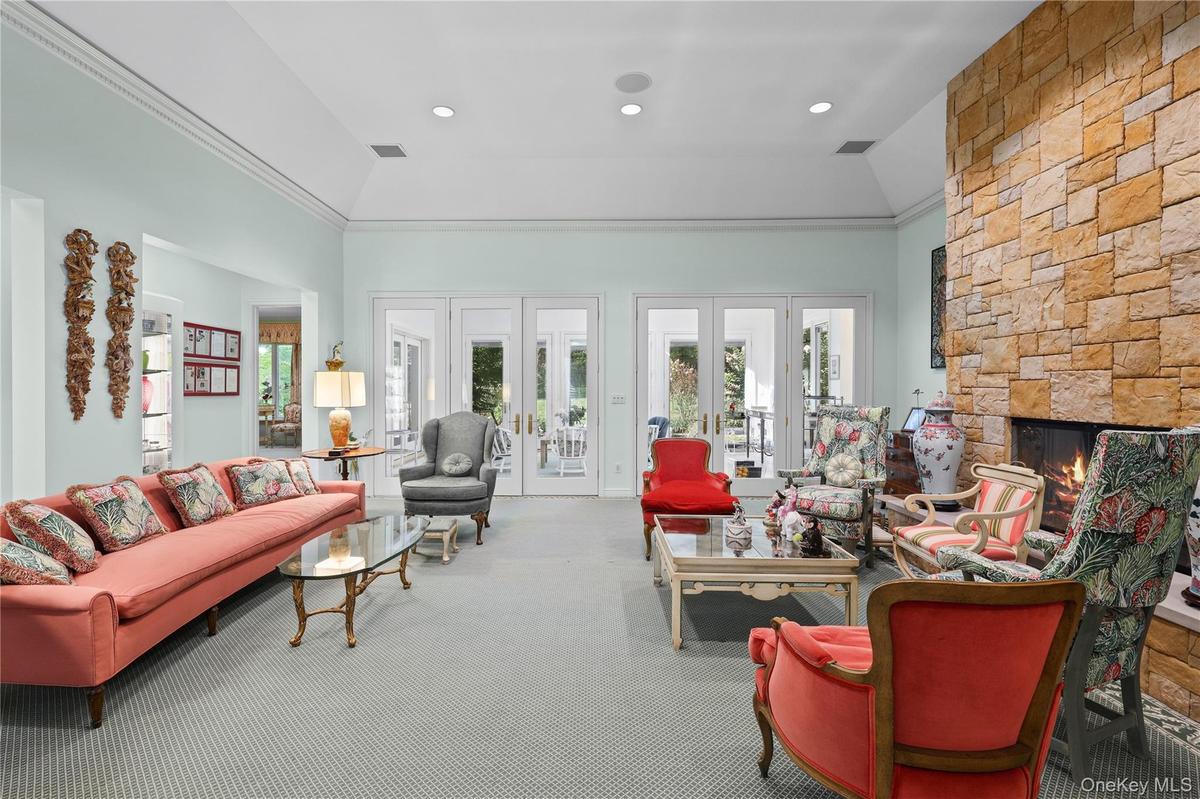 Living area featuring a floor-to-ceiling natural stone fireplace, vaulted ceilings, crown molding, recessed lighting, and multiple sets of glass-paned