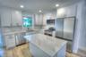 Kitchen featuring white shaker-style cabinetry, stone-patterned countertops, a central island, stainless steel appliances, and wood-finish flooring