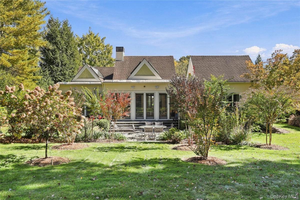 Rear exterior featuring a multi-gabled roofline, stone patio, glass-paned double doors, and established landscaping