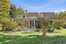 Rear exterior featuring a multi-gabled roofline, stone patio, glass-paned double doors, and established landscaping
