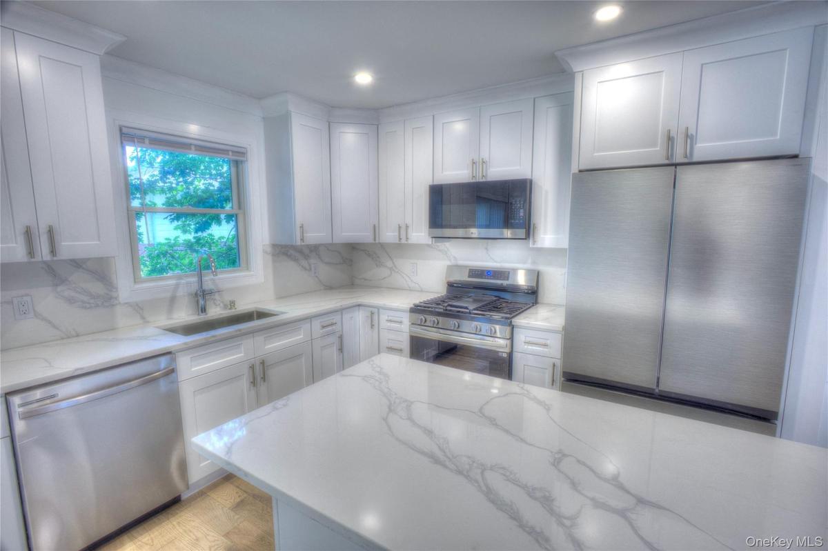 Kitchen featuring white cabinetry, stone-finish countertops with veining, full-height stone-finish backsplash, stainless steel appliances, and a cente