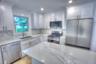 Kitchen featuring white cabinetry, stone-finish countertops with veining, full-height stone-finish backsplash, stainless steel appliances, and a cente