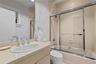 Bathroom featuring a vanity with a drop-in sink, chrome fixtures, a tiled tub-shower combination with glass sliding doors, and patterned wall covering